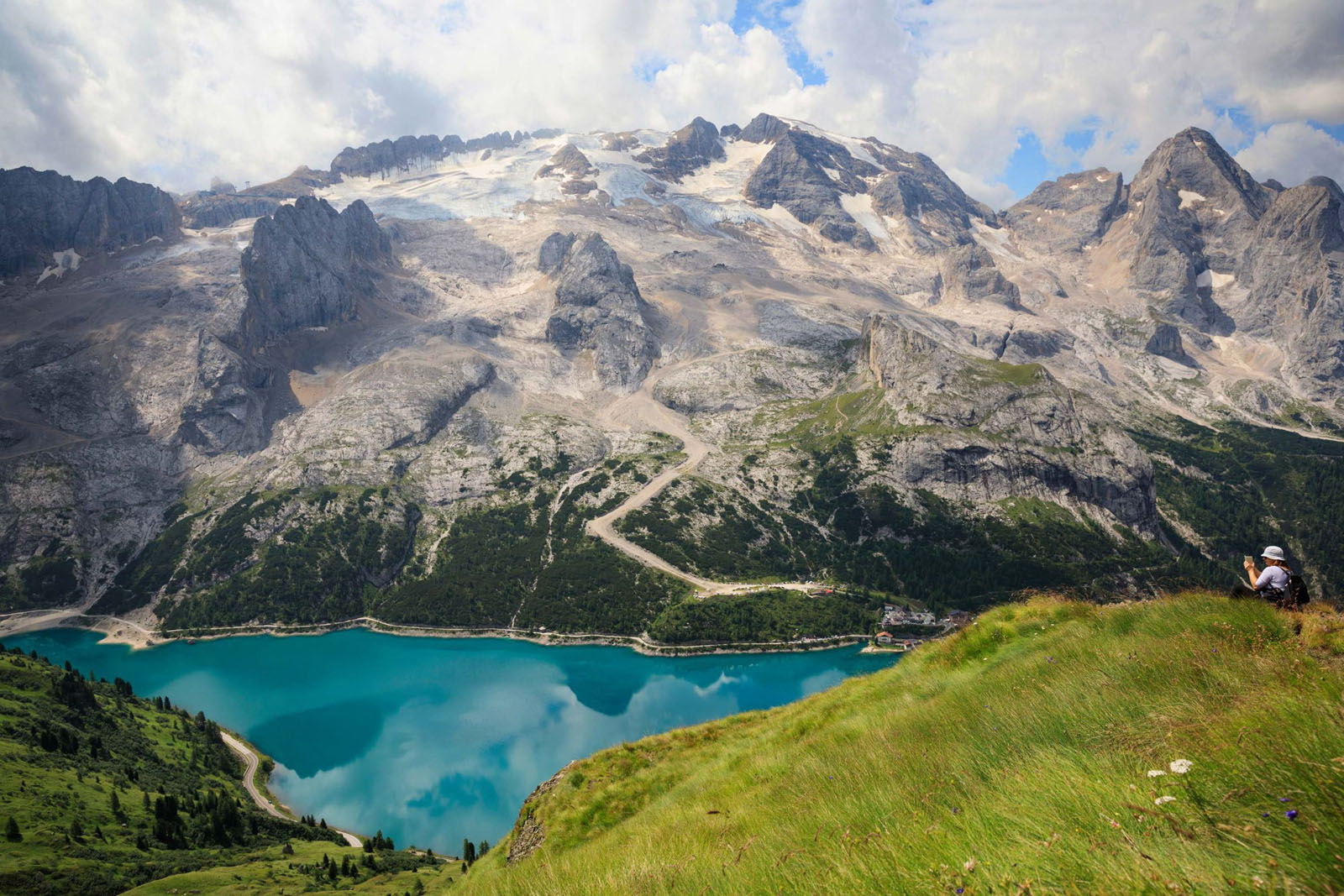 Senior woman enjoying Beautiful view of lake Fedaia and Marmolada mountain from resting point on path from Fedaia pass to pass Pordoi in Dolomites, Northern Italy. Summer on the mountain Arabba.