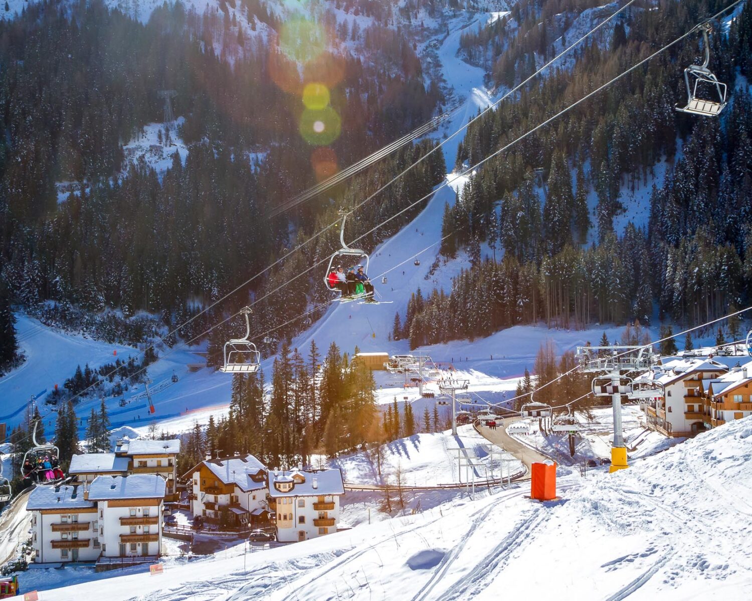 View of Arabba village and chair lift with skiers on a sunny winter day. Sellaronda, Dolomiti Superski.