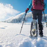 A woman with a backpack in snowshoes climbs a snowy mountain